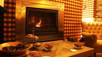 A cozy room with a fireplace, checkered walls, a tufted armchair, and a dining table with various dishes.