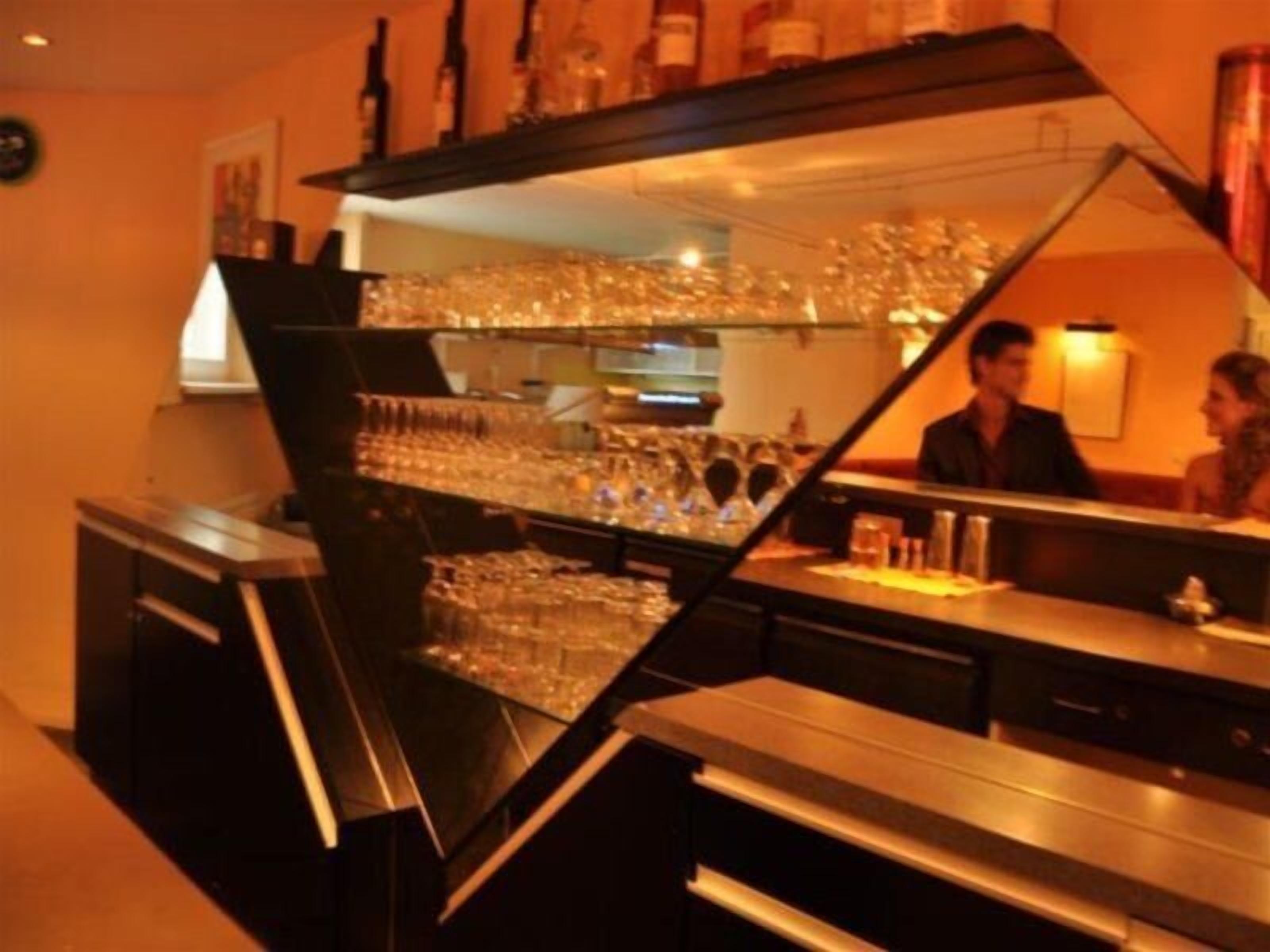 A bar area with a counter, shelves with glasses, and bottles.