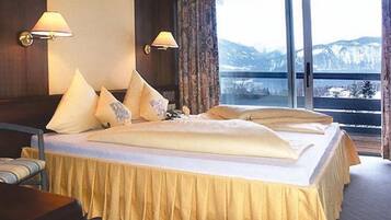 A hotel room with a large bed, two bedside lamps, a view of mountains through a large window, and a curtain.