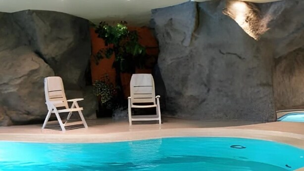 A swimming pool with two white lounge chairs and a rock wall backdrop. - Belmont (Imst)