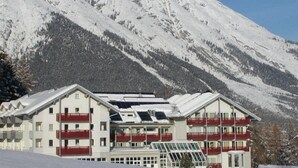 A multi-story hotel with a symmetrical facade, balconies, and a ski slope in the foreground. - Belmont (Imst)