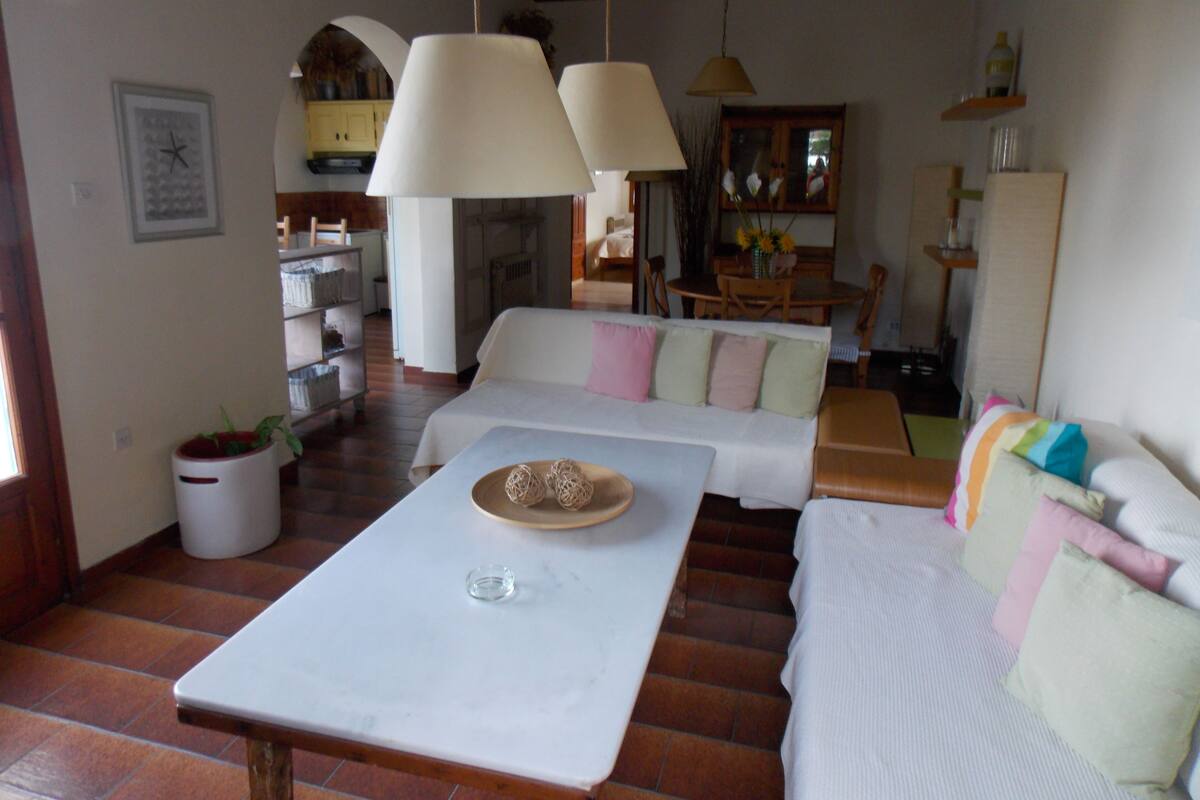 A cozy living room with a white sofa, a coffee table, and a dining area with a wooden table and chairs.