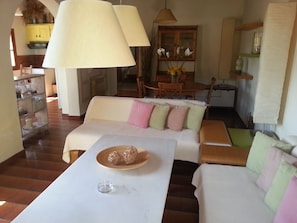 A cozy living room with a sofa, a coffee table with decorative items, and a dining area with a table and chairs. - Studios and Suites Rania (Mykonos)