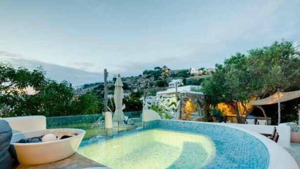 Zona de piscina con fuente, rodeada de mobiliario exterior y vistas a una colina.