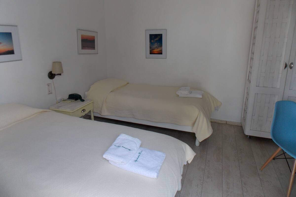 A hotel room with two beds, a wardrobe, and two framed pictures on the wall.