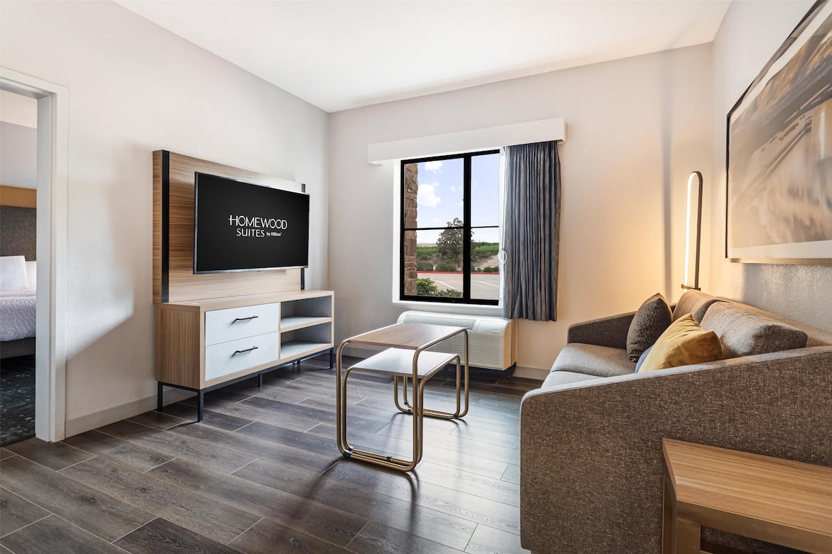 A modern hotel room with a flat-screen TV, a sofa, a coffee table, and a large window with a view.