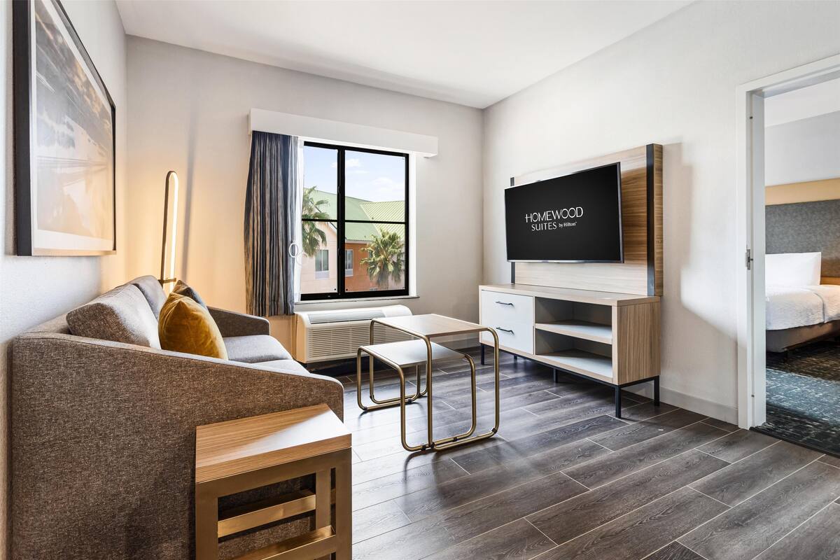 A modern hotel room with a sofa, a TV, a desk, and a bed.