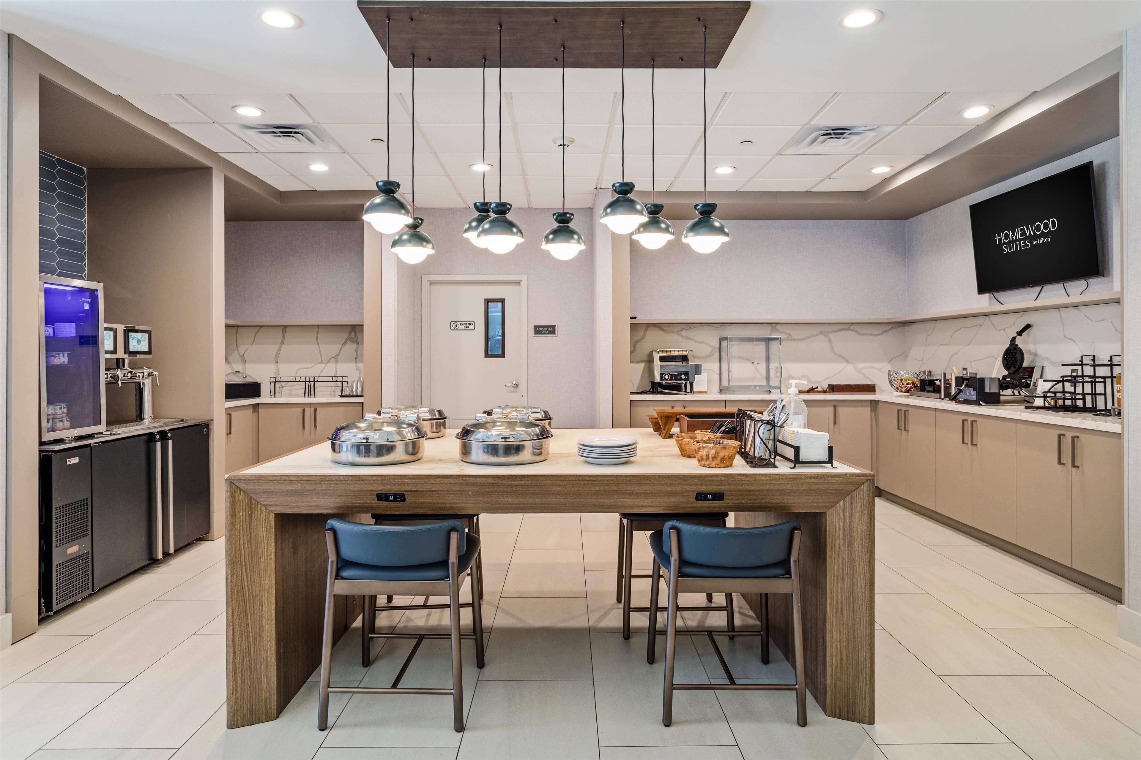 A modern kitchen with a central island, two blue chairs, and overhead pendant lighting.