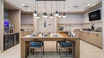 A modern kitchen with a central island, two blue chairs, and overhead pendant lighting.