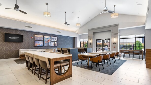 A modern hotel lobby with a large dining area, multiple ceiling fans, and artwork on the walls. - Homewood Beaumont, TX (Beaumont)