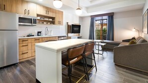 A modern kitchen with wooden cabinets, a stainless steel refrigerator, and a central island with bar stools. - Homewood Beaumont, TX (Beaumont)