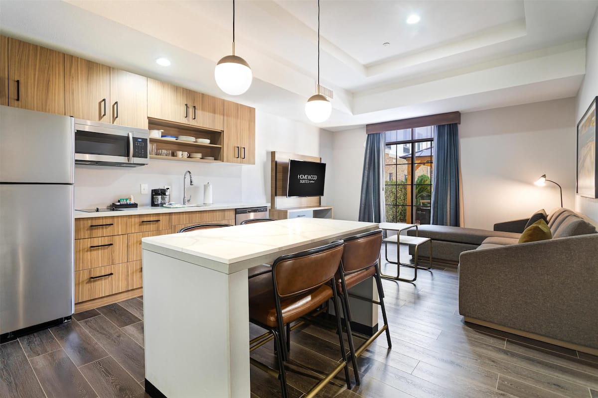 A modern kitchen with wooden cabinets, a stainless steel refrigerator, and a central island with bar stools.
