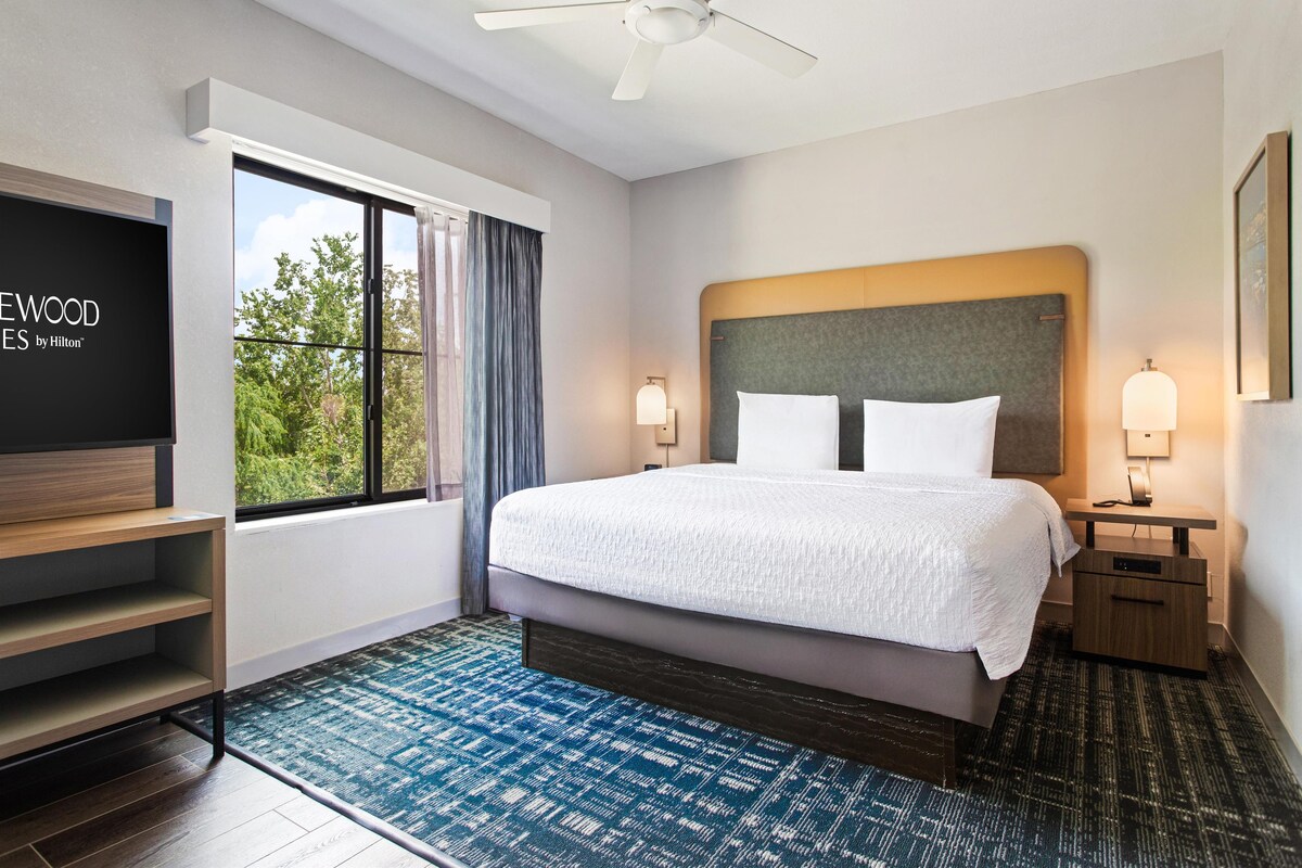 Une chambre d’hôtel avec un lit, une télévision, un bureau et une fenêtre avec des rideaux.