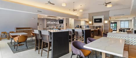 A modern hotel lobby with a bar area, seating, and a television screen.