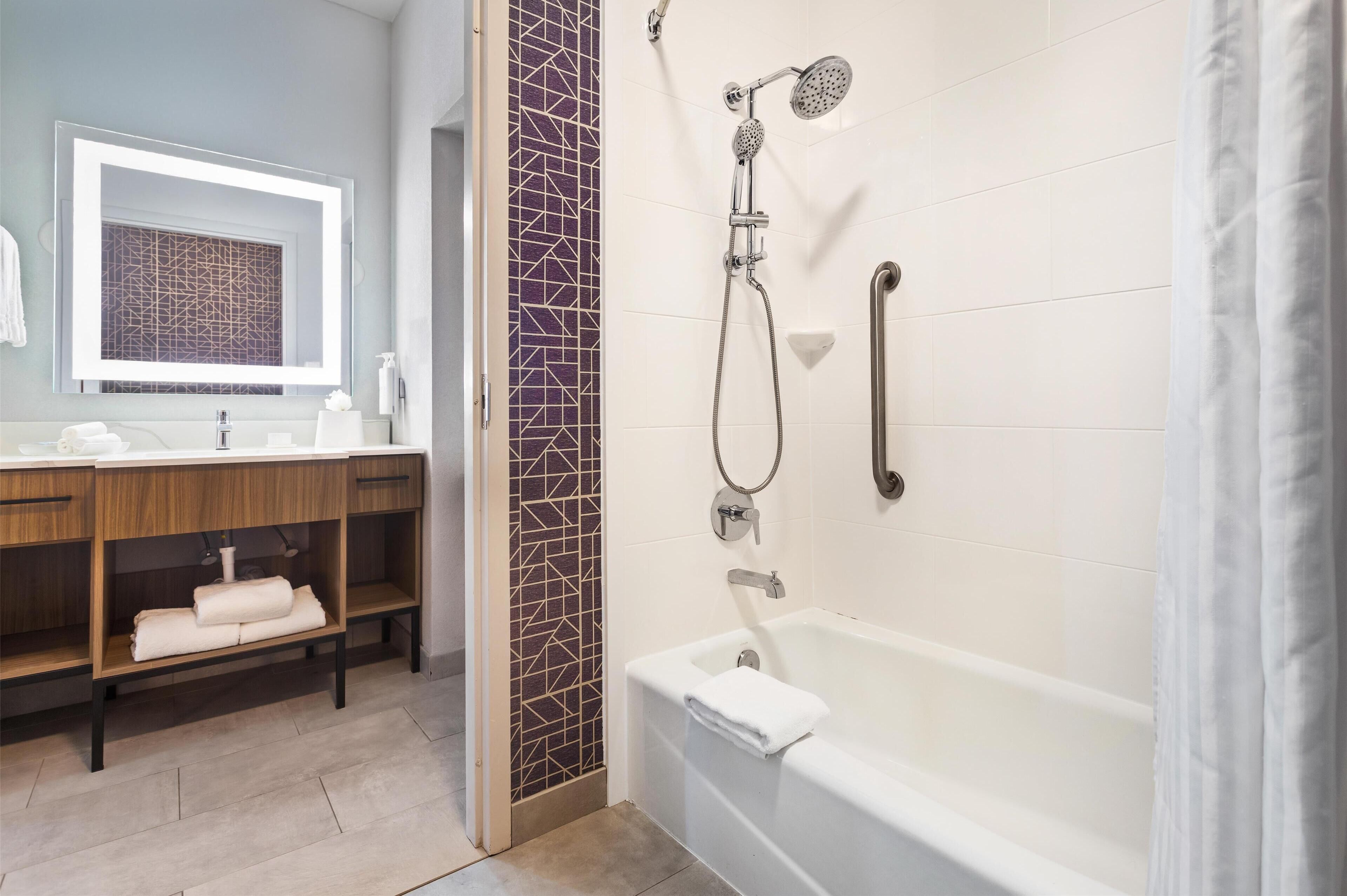 A bathroom with a bathtub, a shower, a vanity with a mirror, and a towel rack.