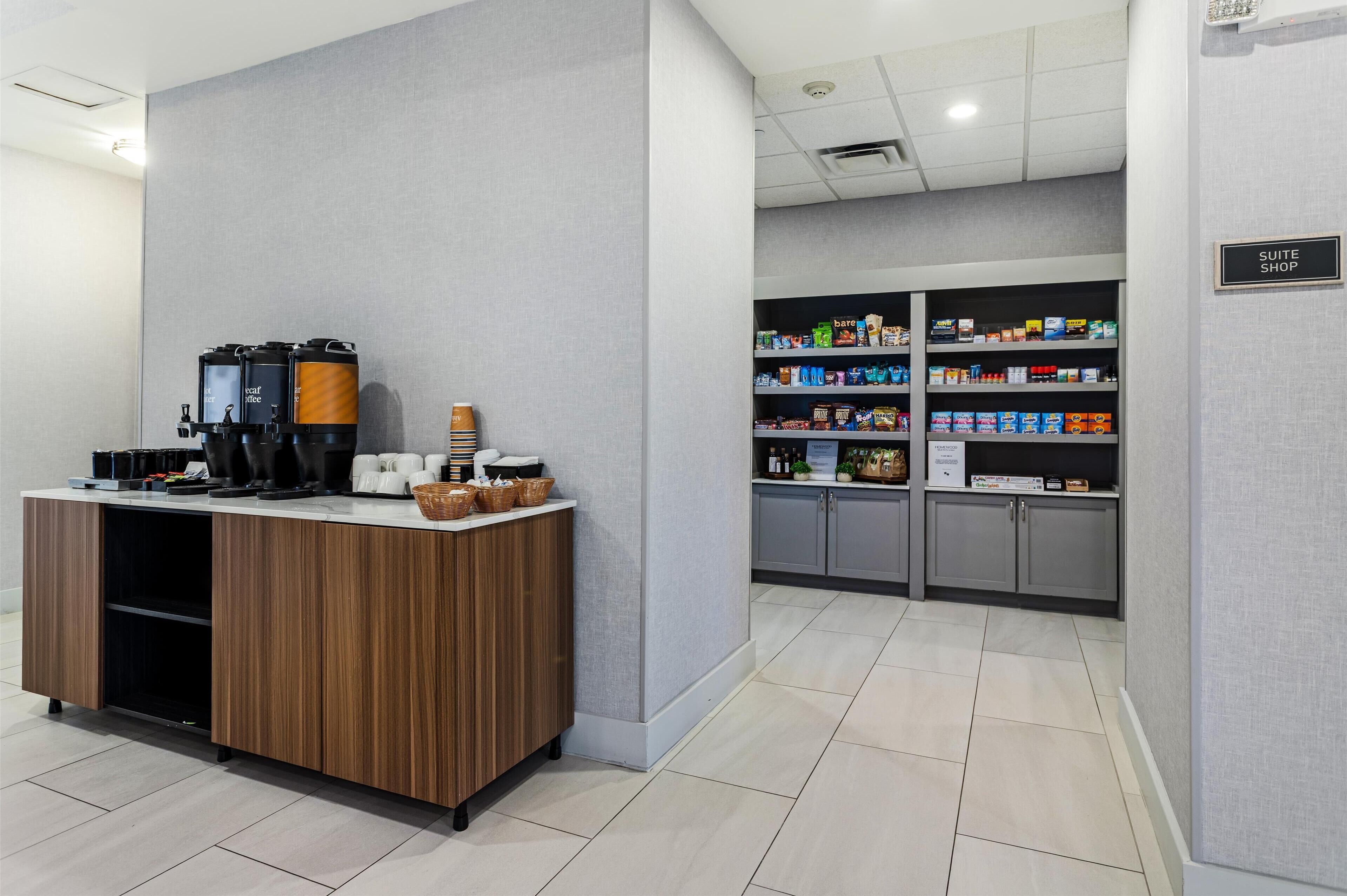 En hotellobby med en kaffestation, en skylt som visar vägen till hotellets butik och hyllor fyllda med snacks och drycker.