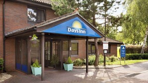 A Days Inn hotel with a covered entrance, brick facade, and outdoor seating area with planters. - Days Inn by Wyndham Southampton Rownhams (Southampton)