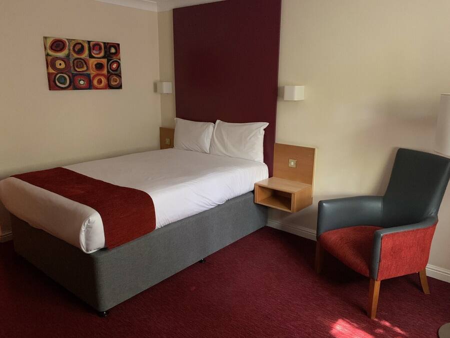 Ett hotellrum med en säng, en stol, ett nattduksbord och en tavla på väggen.