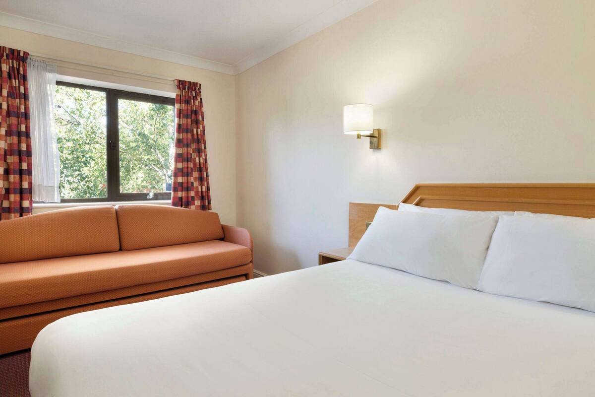 Une chambre d’hôtel avec un grand lit, un canapé, une table de chevet et une fenêtre avec des rideaux.
