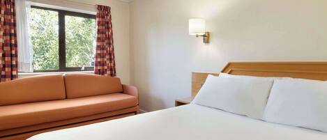 A hotel room with a large bed, a sofa, a nightstand, and a window with curtains.