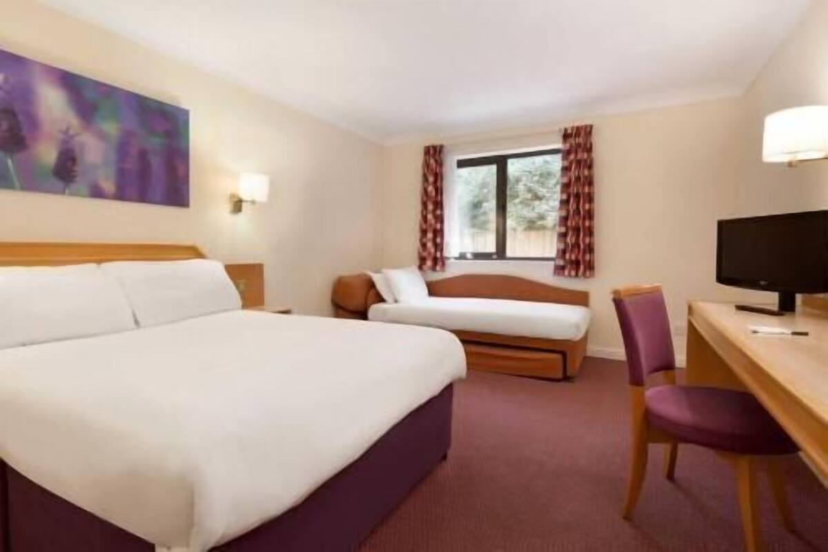 Une chambre d’hôtel avec un grand lit, un bureau avec une chaise, une télévision et une fenêtre avec des rideaux.