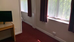 A room with a desk, two windows with curtains, a carpeted floor, and a door leading to another room. - Days Inn by Wyndham Southampton Rownhams (Southampton)