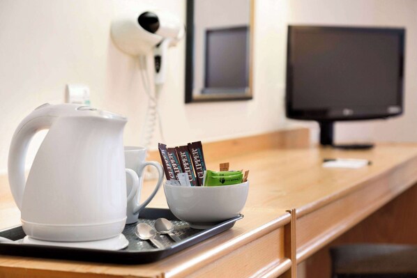 Una estación de café con un hervidor blanco, una taza y un bol que contiene sobres de café y un paquete verde sobre una bandeja.
