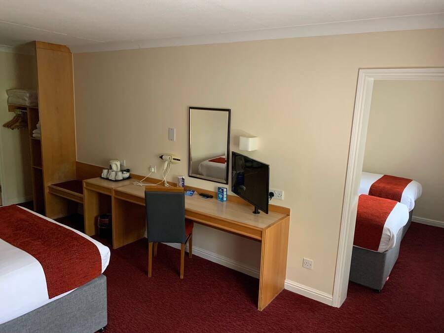 A hotel room with a wooden desk, a chair, a bed with red and white bedding, a mirror, and a wardrobe.