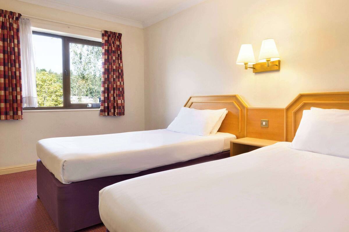 Une chambre d’hôtel avec deux lits, une fenêtre avec des rideaux et des lampes fixées au mur.