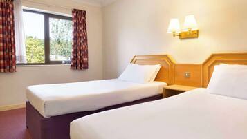 A hotel room with two beds, a window with curtains, and wall-mounted lamps.