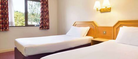 Habitació d'hotel amb dos llits, una finestra amb cortines i làmpades penjades a la paret.