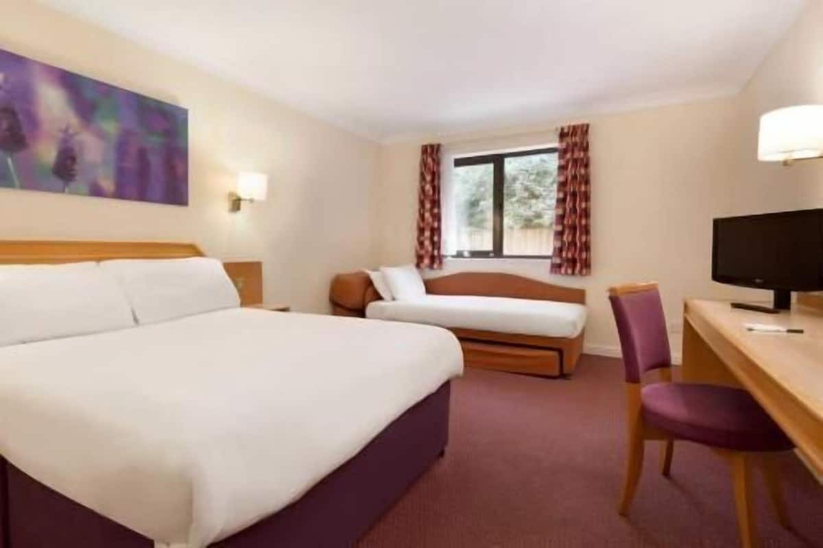 Une chambre d’hôtel avec un grand lit, un bureau avec une chaise, une télévision et une fenêtre avec des rideaux.