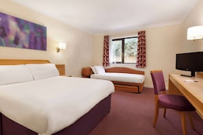 Habitación de hotel con una cama grande, una cama más pequeña, un escritorio con silla, un televisor y una ventana con cortinas.