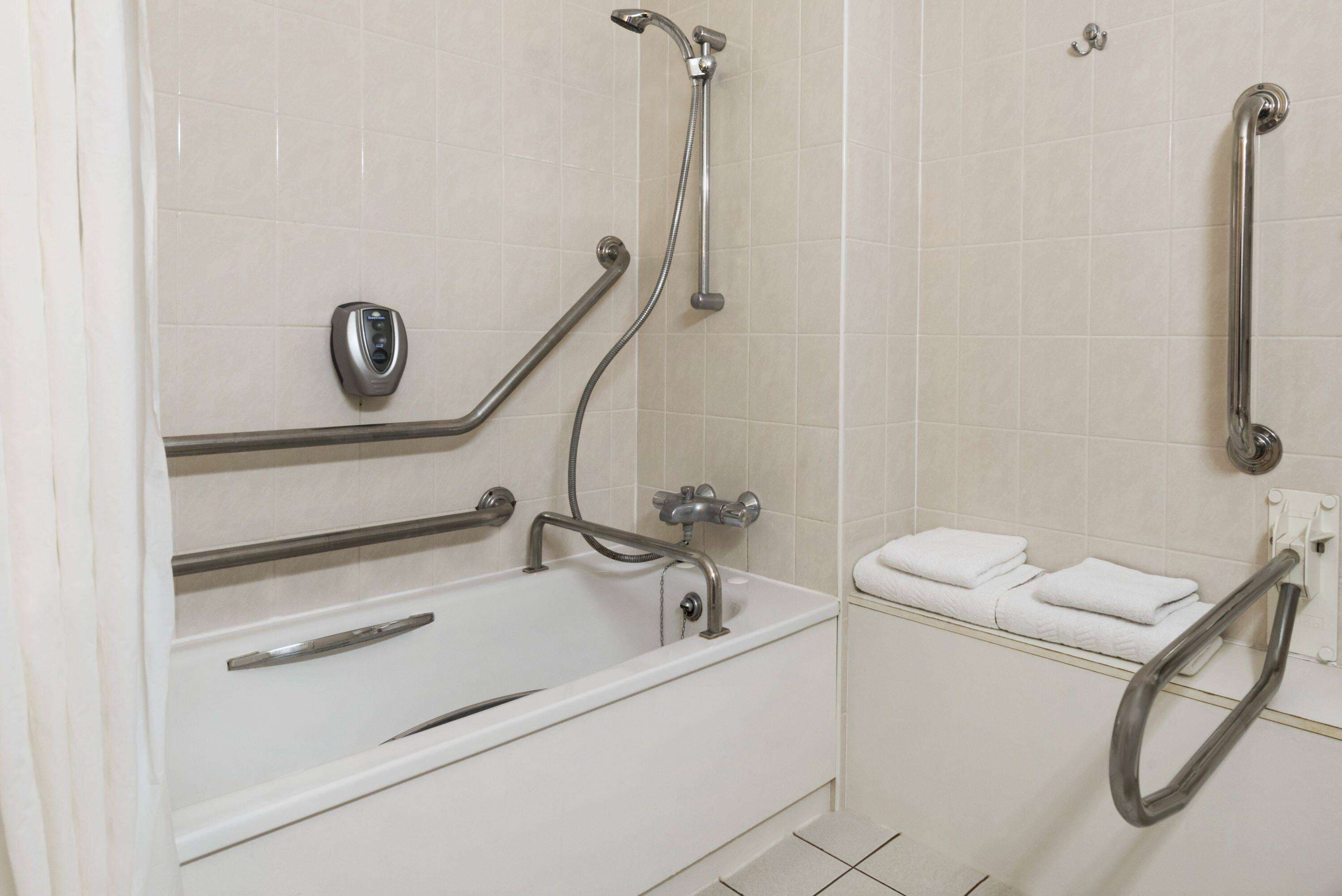 A bathroom with a white bathtub, grab bars, a towel rack, and a handheld showerhead.