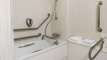 Ein Badezimmer mit einer weißen Badewanne, Haltegriffen, einem Handtuchhalter und einer Duschbrause.