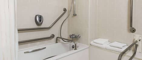 A bathroom with a white bathtub, grab bars, a towel rack, and a handheld showerhead.