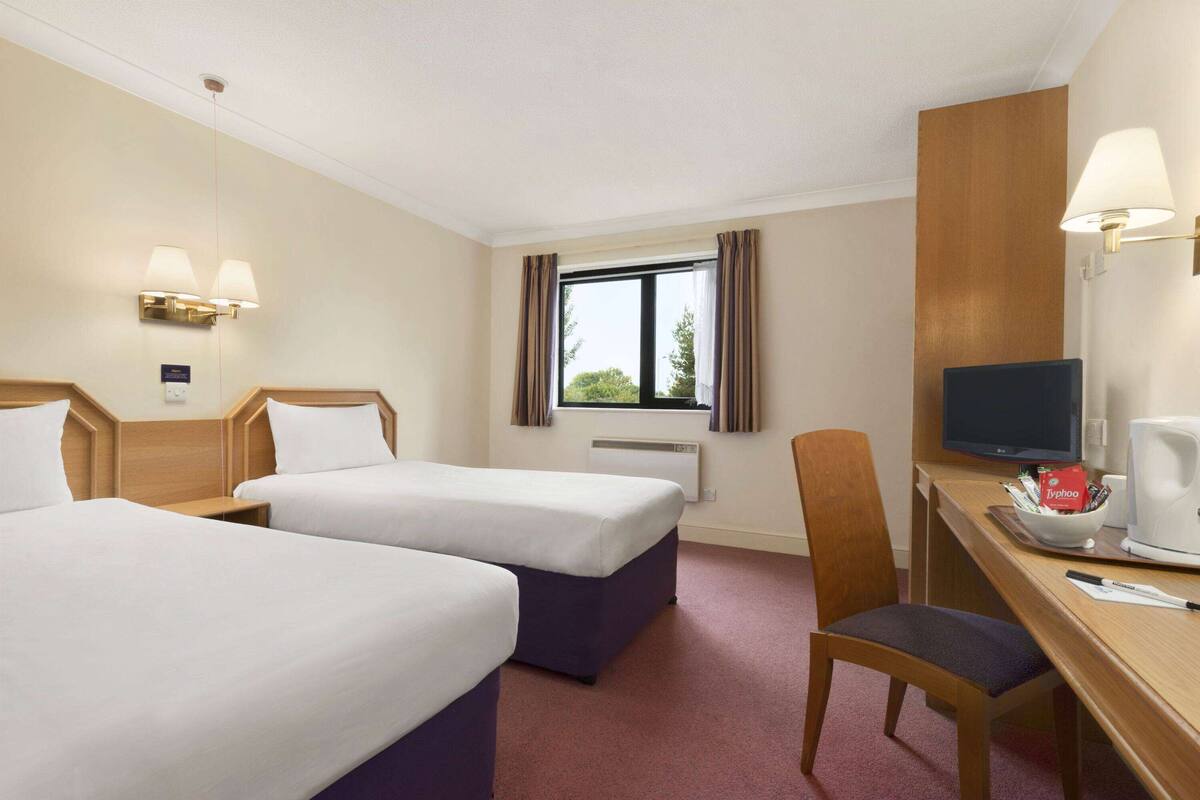 Ett hotellrum med två sängar, ett skrivbord med en tv, en stol och ett fönster med gardiner.