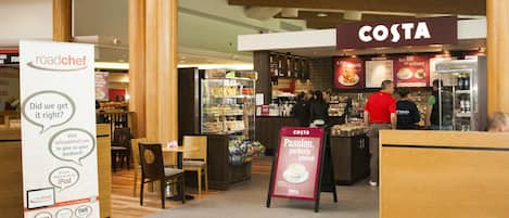 A Costa coffee shop with a visible menu board, a promotional stand, and a seating area with wooden furniture.