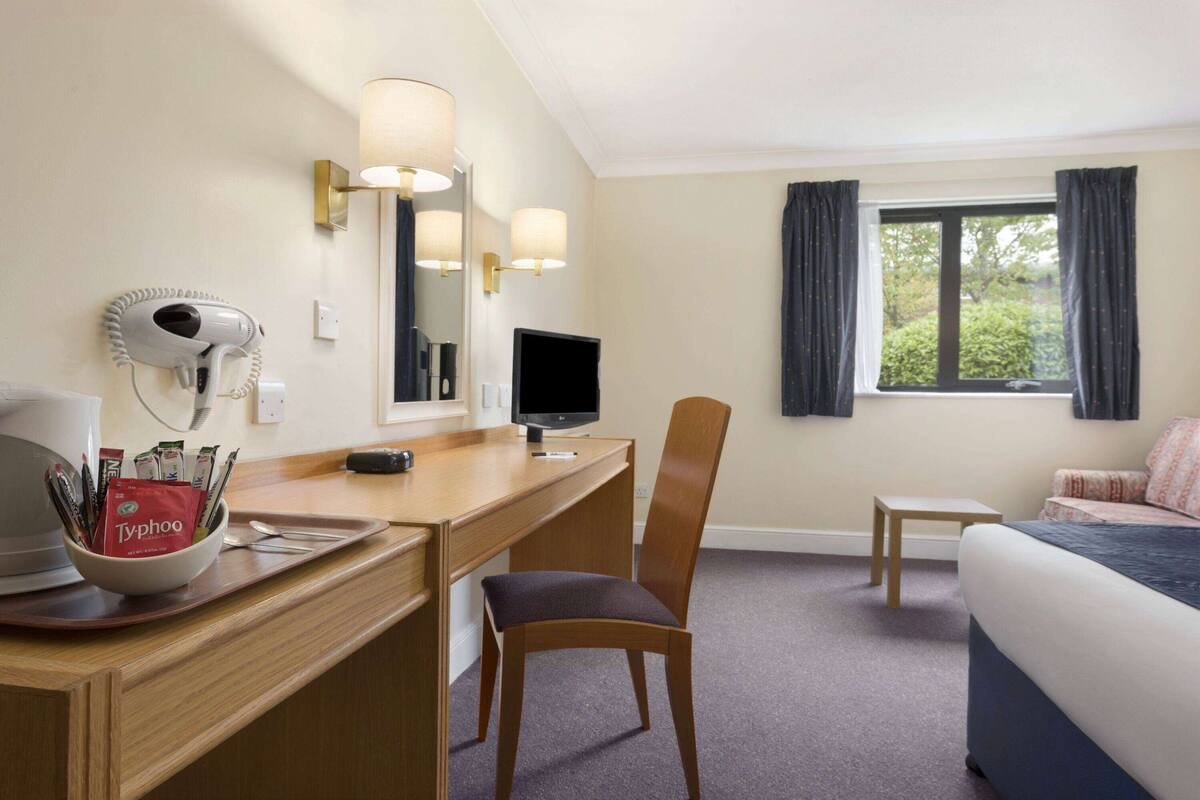 Ett hotellrum med ett skrivbord, en stol, en säng och ett fönster med gardiner.