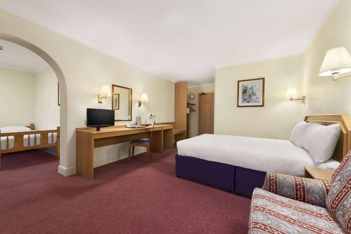 Ett hotellrum med en säng, ett skrivbord med en dator, en stol och en tv.