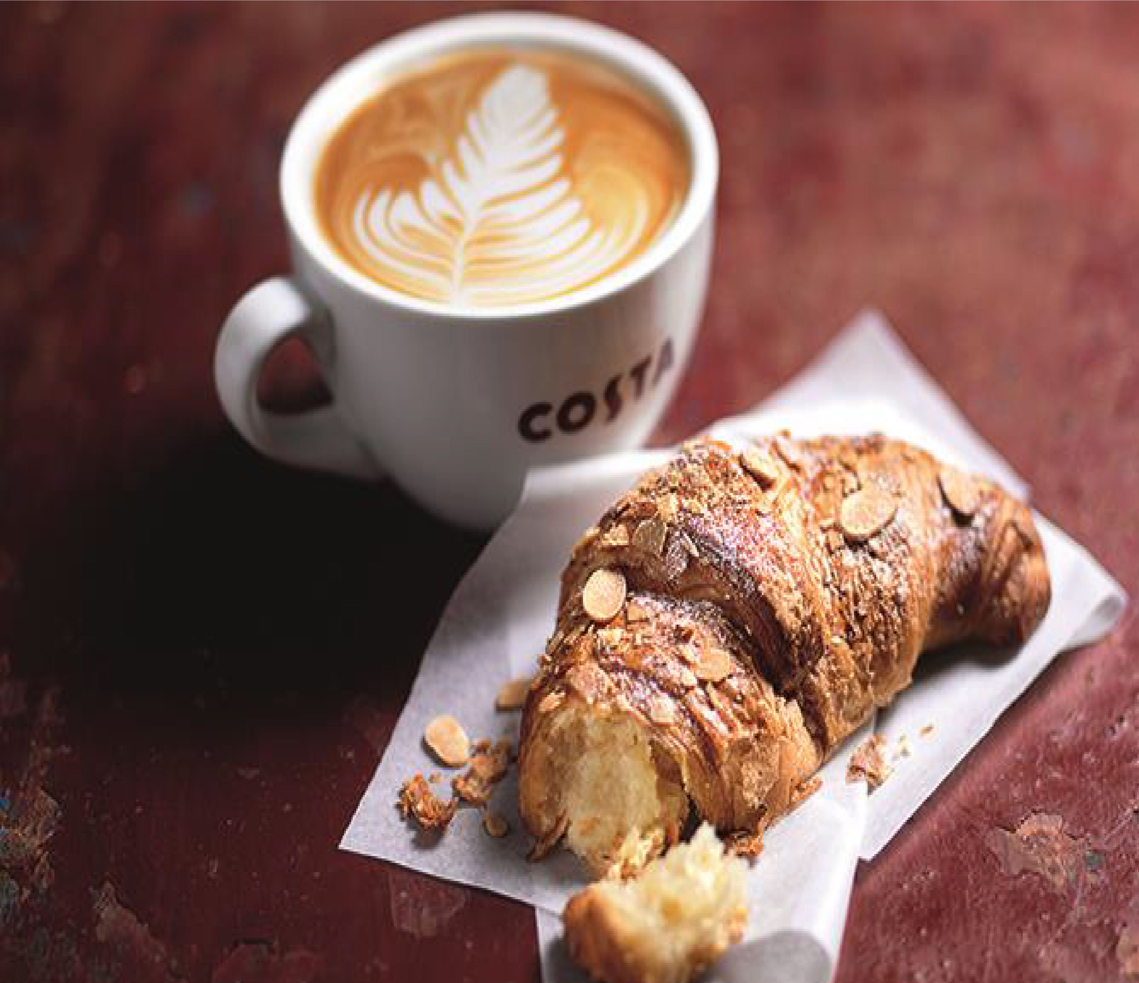 A croissant and a cup of coffee with latte art on a table.