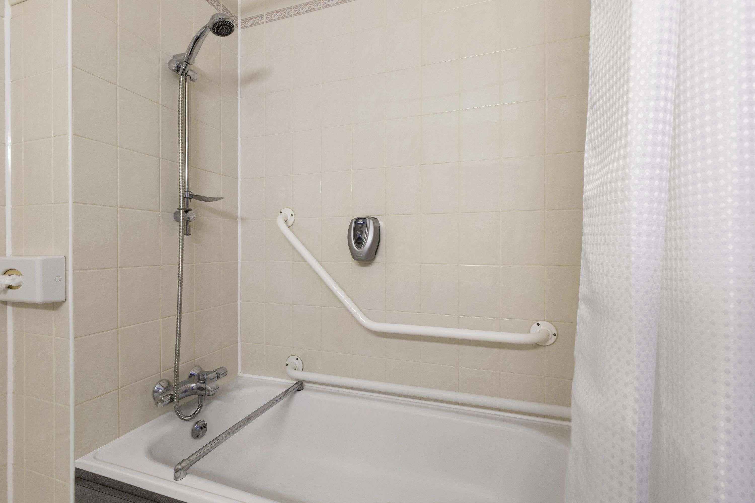 A bathroom with a bathtub, a shower, and a handrail.