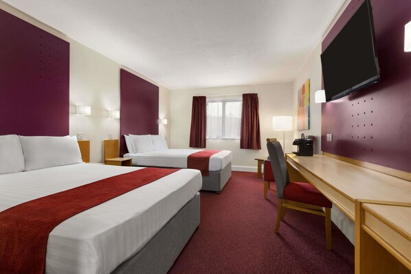 A hotel room with two beds, a desk, a chair, a TV, and a window with curtains.