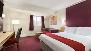 A hotel room with a bed, a desk, a chair, a small table, and a window with curtains.
