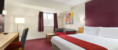 A hotel room with a bed, a desk, a chair, a small table, and a window with curtains.
