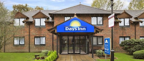 Een Days Inn hotel met een gevel van baksteen, een blauw bord en een verzorgd gazon.