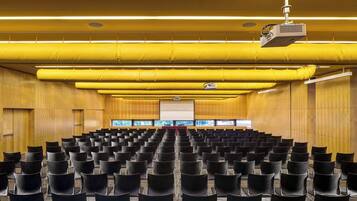 Un salón de conferencias con filas de sillas, un proyector y una pantalla.