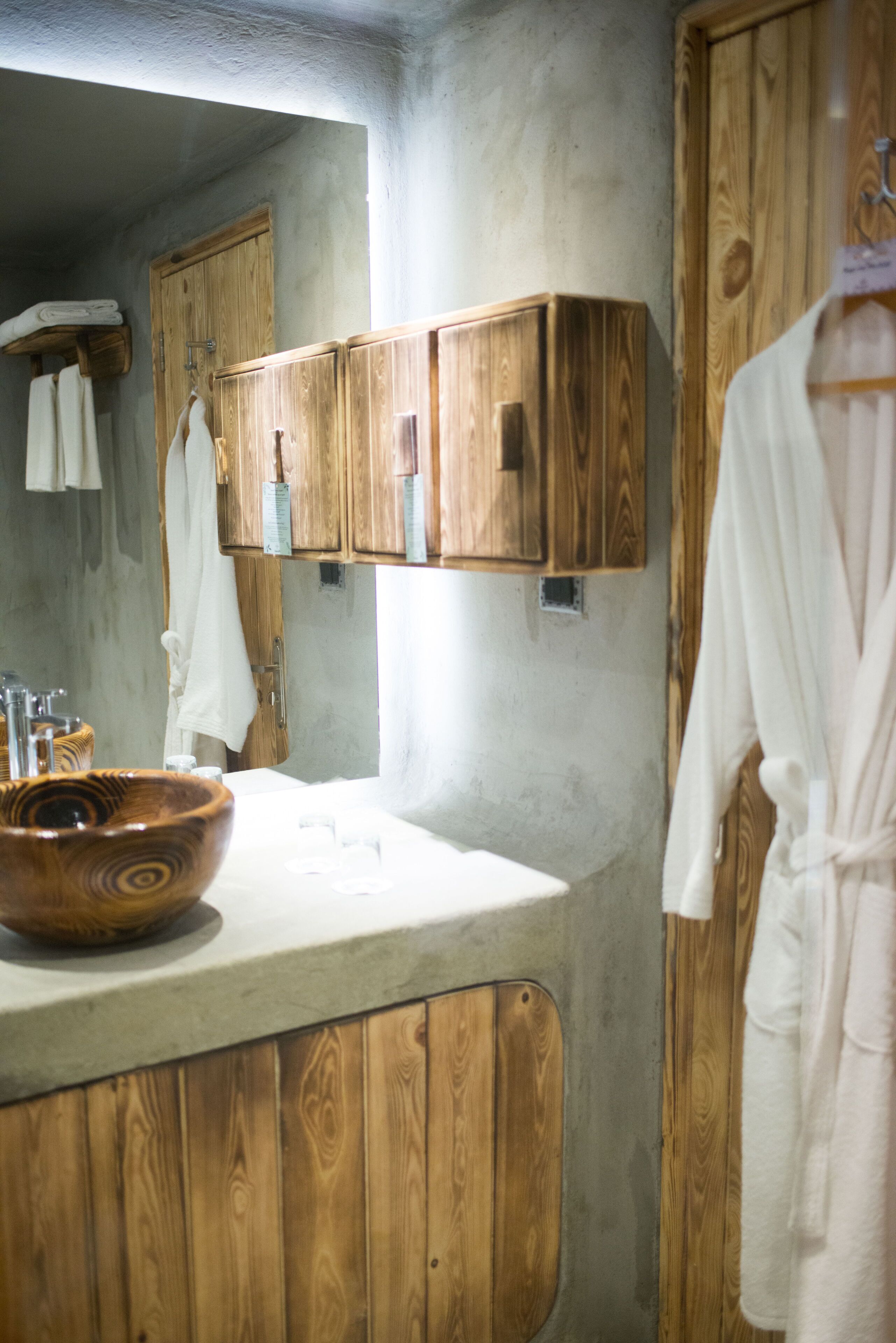 A bathroom with wooden cabinets, a wooden bowl sink, and a white robe hanging on the wall.
