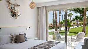 A modern hotel room with a large bed, a dreamcatcher decoration, and a view of a tropical garden through the glass door.