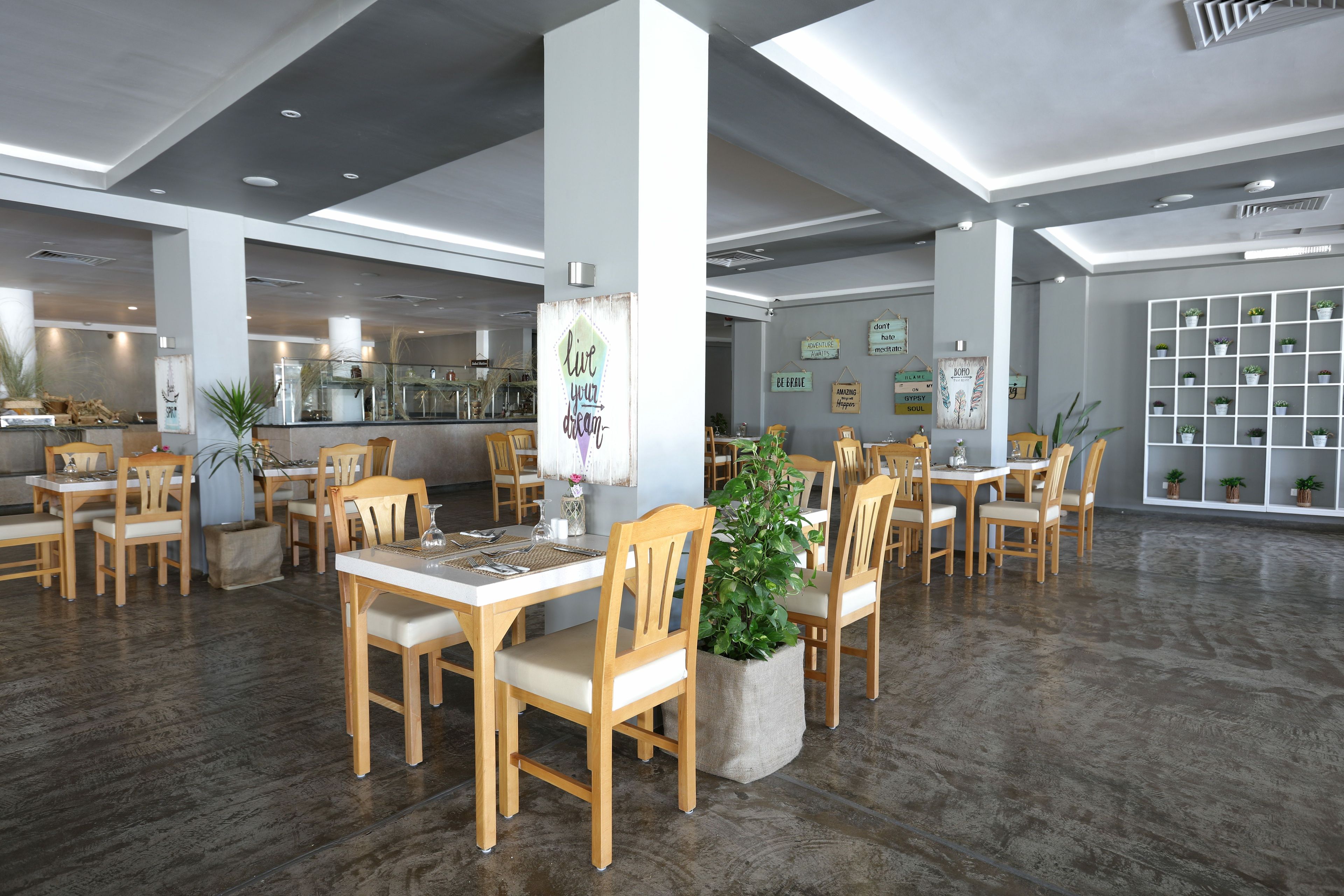 Un comedor moderno con mesas y sillas de madera, una columna central y una pared con citas motivacionales.